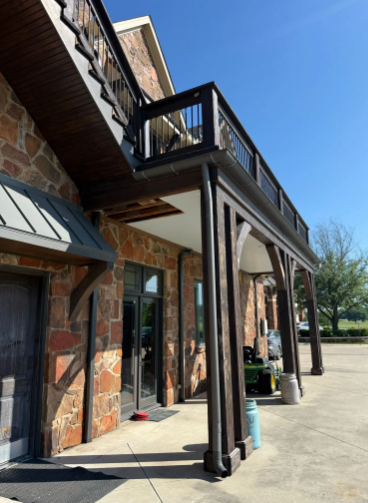 Exterior of a building with brick and wooden accents, a second-story balcony, and a covered entrance.