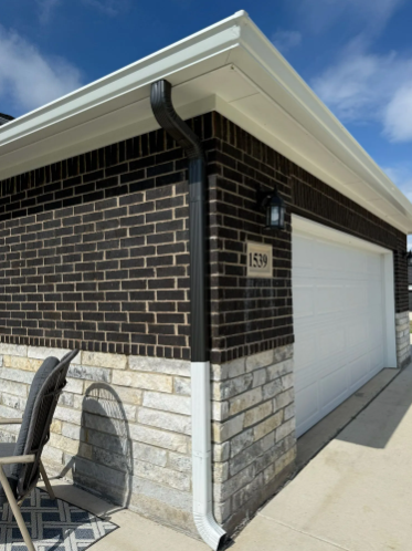 Garage with black brick upper wall, white garage door, and light stone lower wall with white gutters.