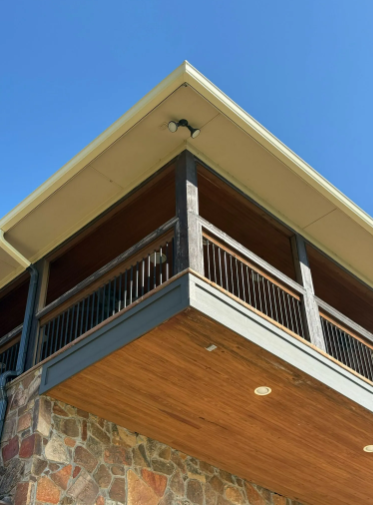 Corner of a building with a wooden balcony, stone base, and a clear blue sky.