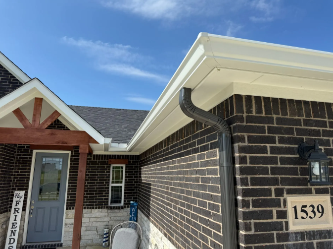 Dark brick house with white trim, dark gutters, and blue sky.