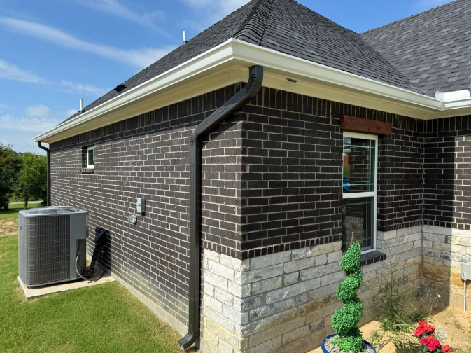 Brick house with dark grey roof, black gutters, and AC unit on the side.