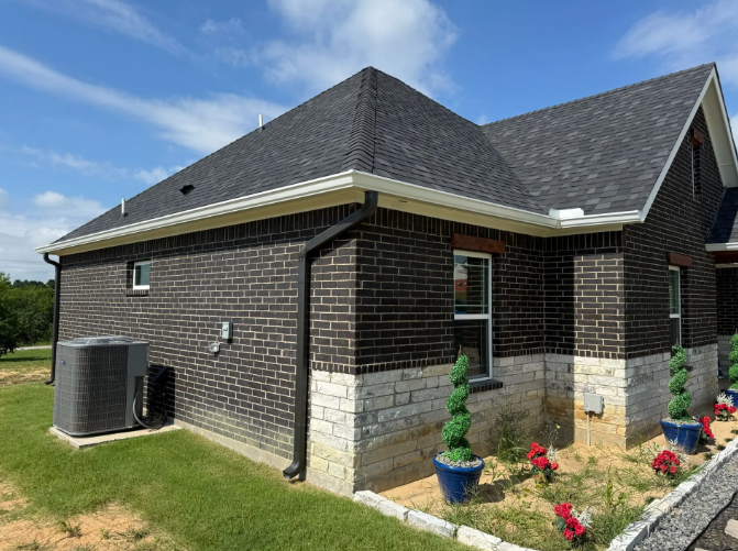 Dark brick house with white trim, black roof, and green lawn on a sunny day.