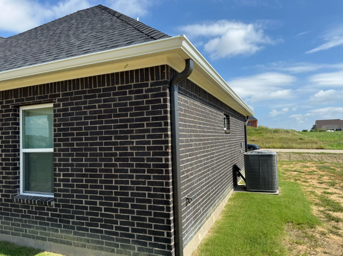 Dark brick building with white trim, black gutters, and an air conditioner unit.