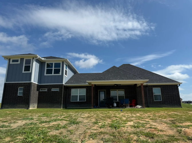 Back exterior of a two-story house with blue and brown siding under a bright blue sky.