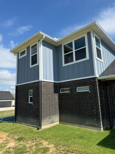 Blue and black brick house with white trim against a blue sky.