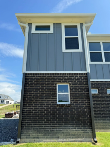 Exterior of a modern building with gray siding above dark brick. Windows are visible.