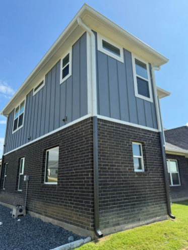 Two-story modern home with brick lower level and gray vertical siding upper level, white trim, and a blue sky.