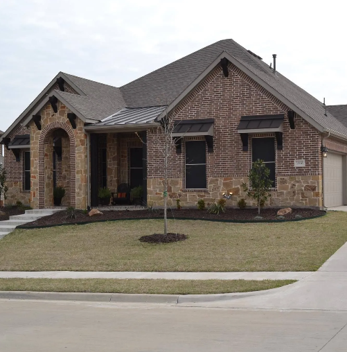 Brick home with stone accents and black awnings over windows. Front yard with brown mulch and green grass.