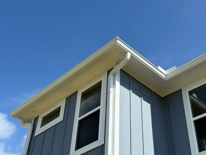 Blue and white house exterior with windows, roofline, and clear blue sky.