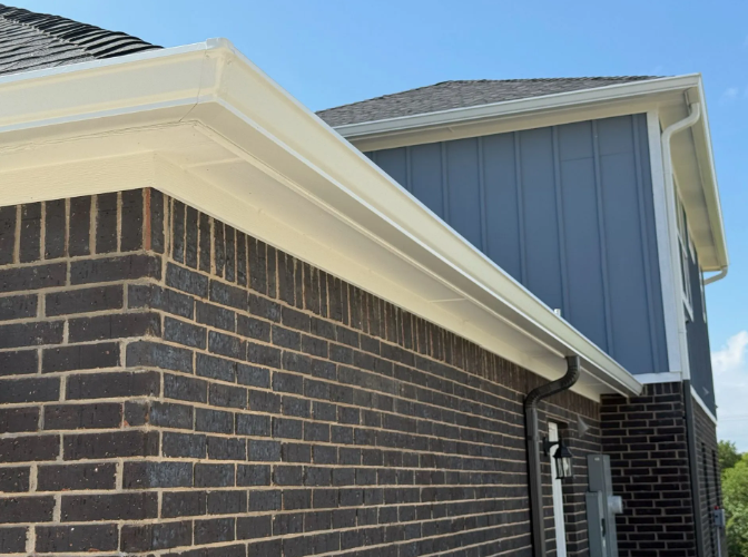 White gutters on a brick home with blue siding against a clear sky.
