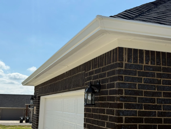 Garage corner with brick exterior, white door, and light-colored trim and gutters against a blue sky.