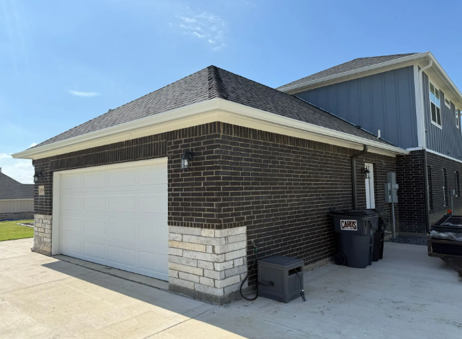 Brick garage with white door and stone accents, connected to a blue-sided house.