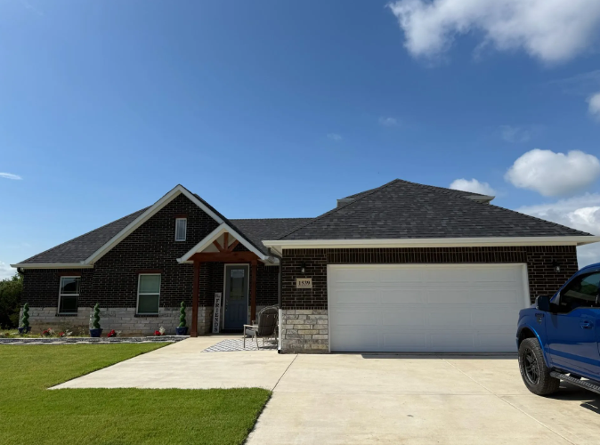 Single-story brick house with a white garage door, concrete driveway, and blue sky.