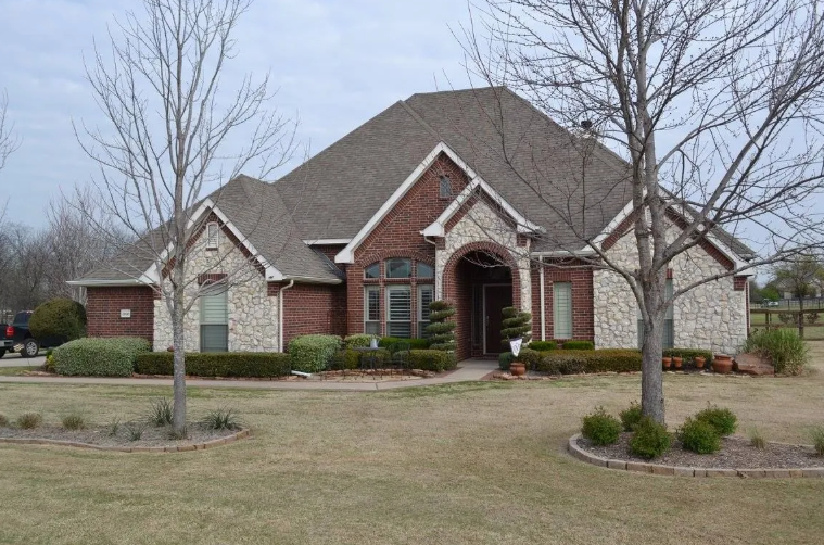 House with red brick and stone facade, brown roof, bare trees, and a front lawn.