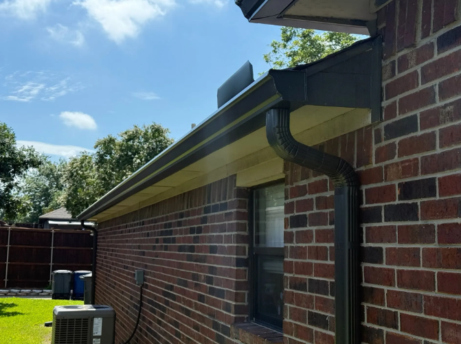 Exterior view of a brick house with dark gray gutters and downspout under a blue sky.