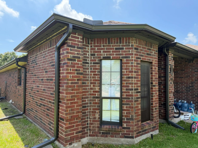 Brick house with dark trim and gutters; blue sky, green grass.