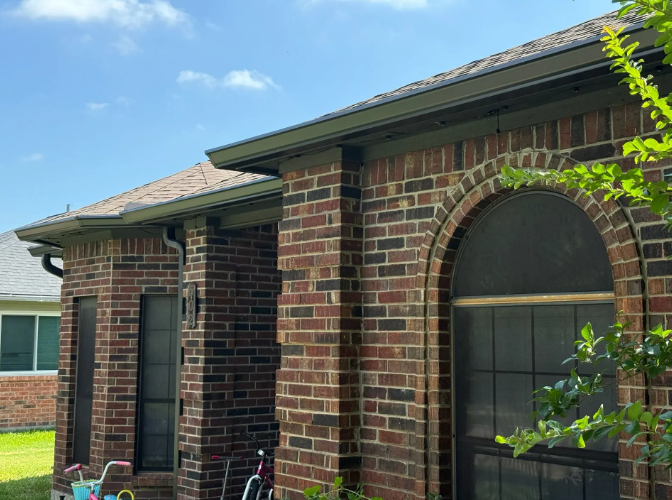 Brick house exterior with dark gutters and a large arched window against a blue sky.