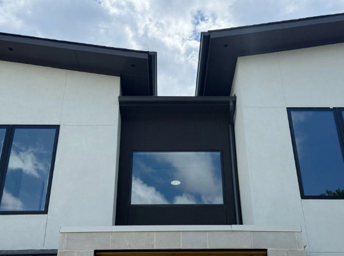 Modern two-story building with white walls, black trim, and large windows reflecting the sky.