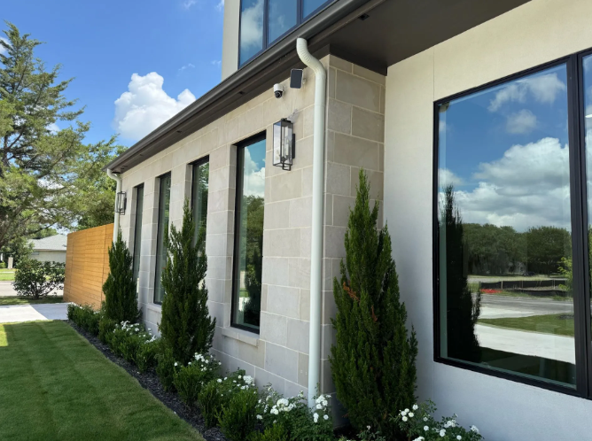 Exterior of a modern building with tall windows, cream-colored stone facade, and landscaping on a sunny day.