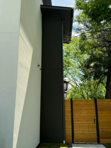 Black exterior wall next to a light gray wall; wooden fence and trees in background.