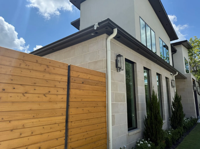 Modern two-story house with light stone exterior, dark trim, and a wooden fence.