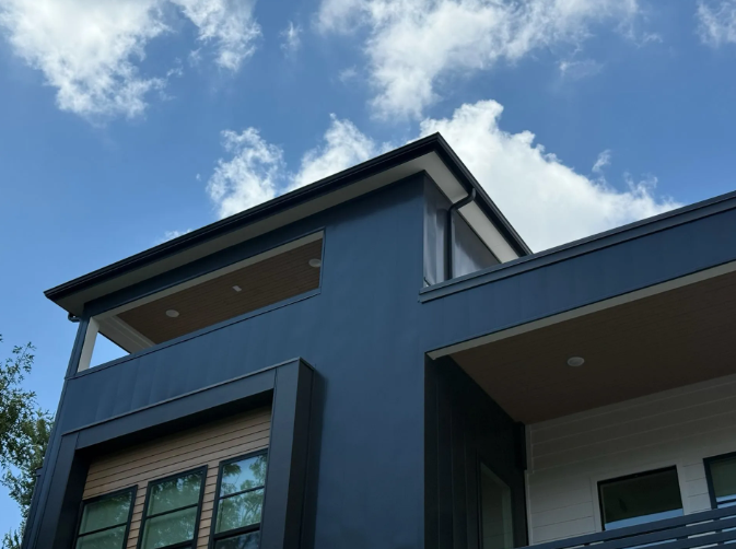 Dark blue modern house against a blue sky with fluffy clouds.
