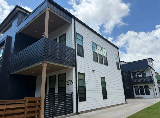 Modern two-story house with white siding and black accents, blue sky background.