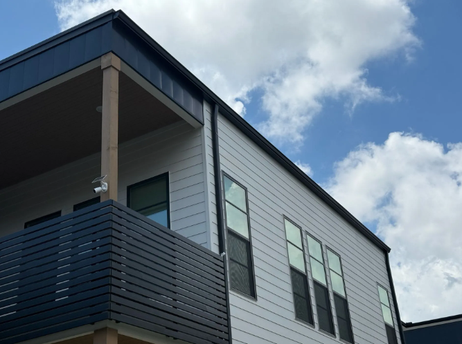 Modern white building with a black balcony and roof against a blue sky with clouds.
