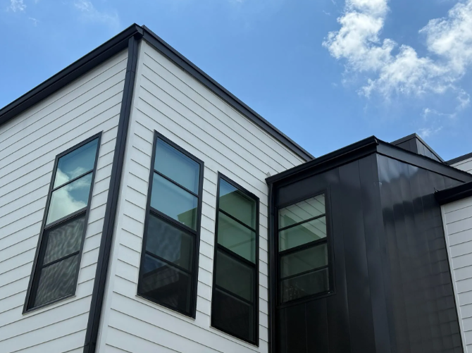 Modern building exterior with white siding, black trim, and large windows against a blue sky.
