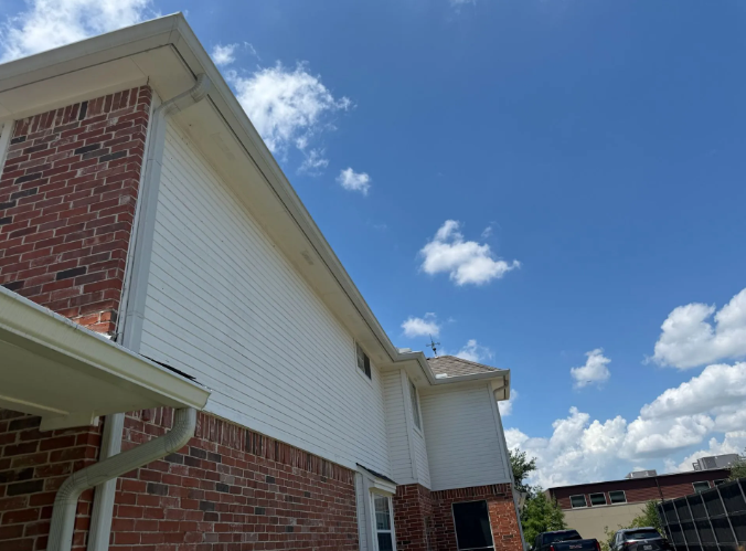 Brick building exterior with white siding, white gutters, and blue sky with clouds.
