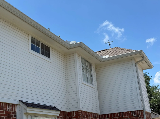White house exterior with gutters, windows, and brick base, under a blue sky.