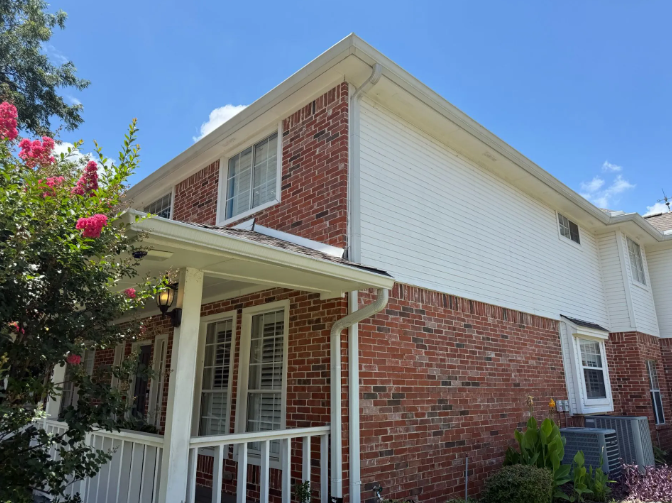 Two-story brick building with white trim, gutters, and windows against a blue sky with clouds.
