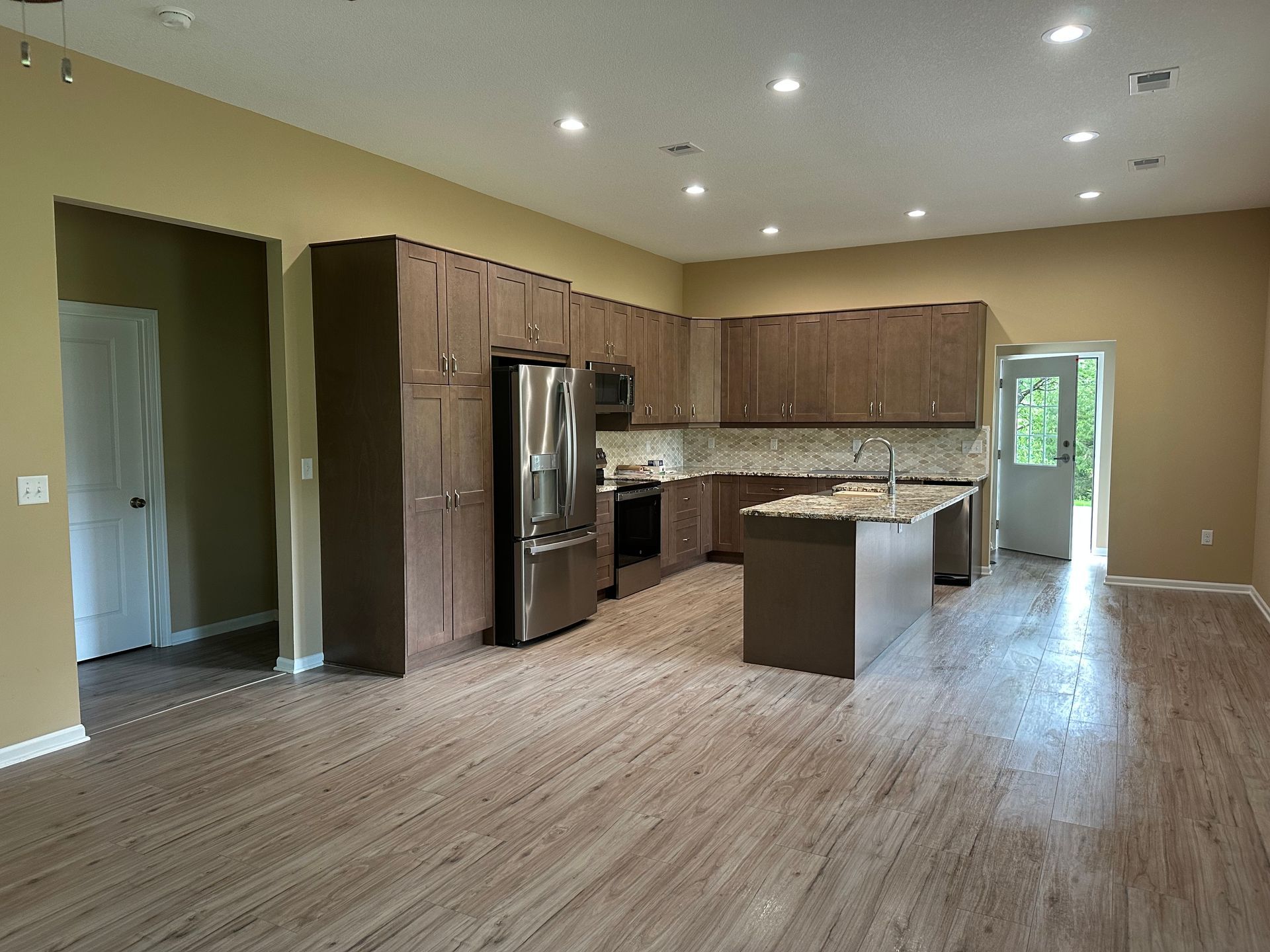 Kitchen with brown cabinets, stainless steel appliances, island, and wood-look flooring.