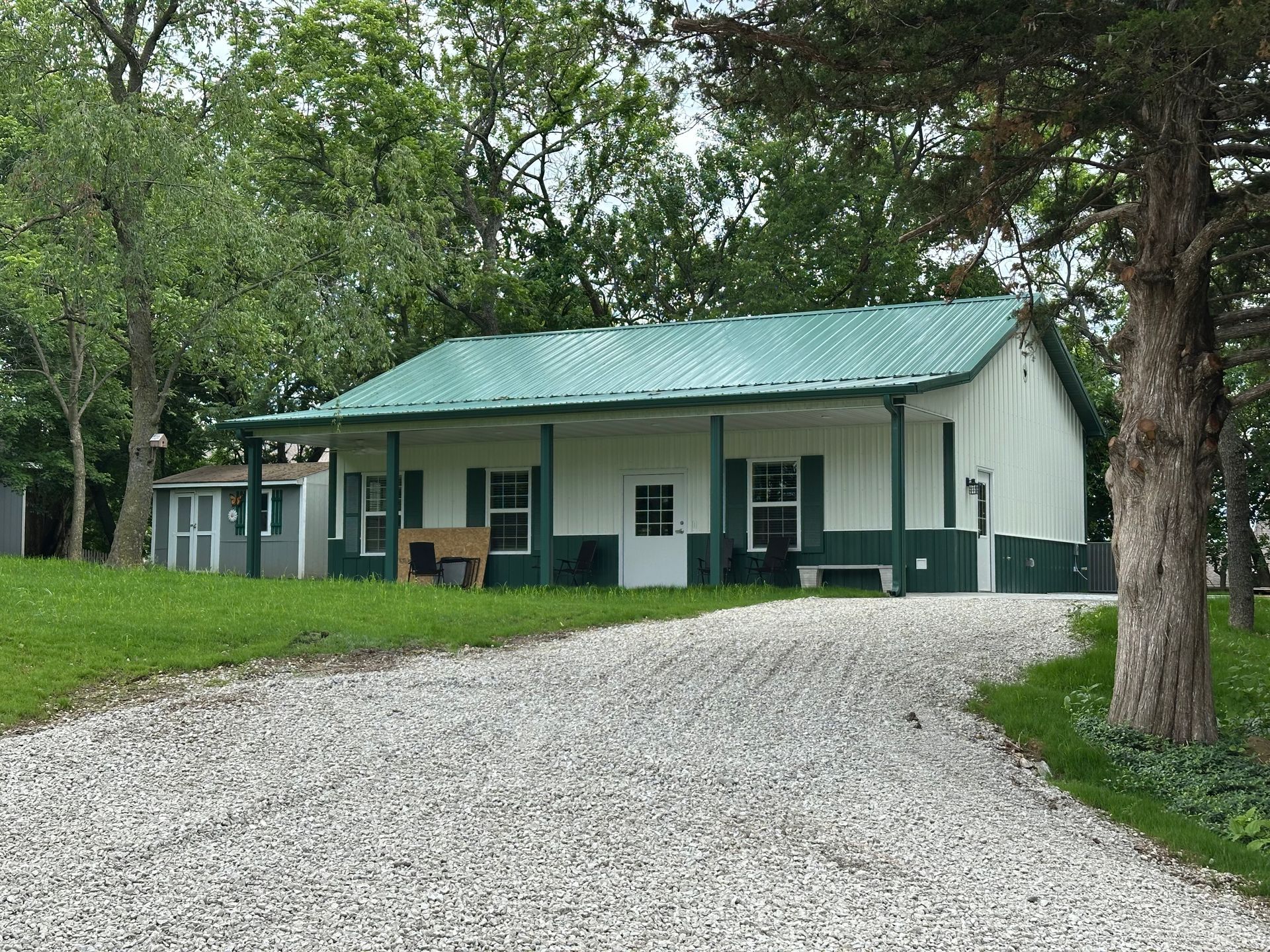 White building with green trim and roof; gravel driveway leading to it.