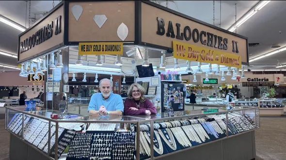 Jewelry store kiosk: two people behind glass displays. Sign reads 