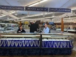 Jewelry store display with two employees behind counters. Signs say, 
