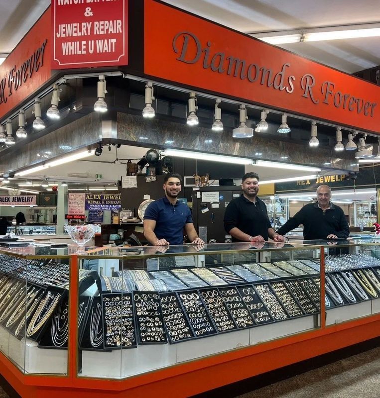 Jewelry store counter with three men behind it, displaying necklaces and other jewelry.