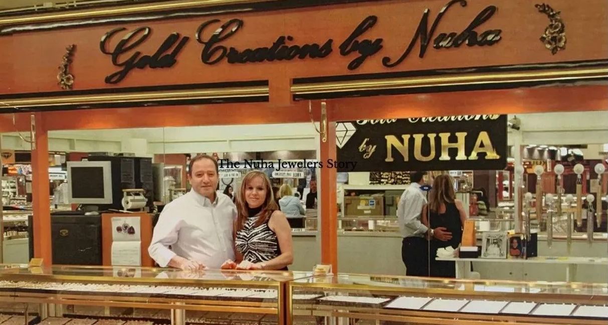 Couple stands behind a jewelry store counter. The store sign says 