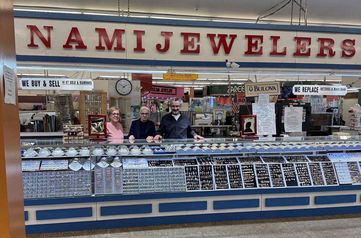 Namie Jewelers storefront with three people behind display cases of jewelry.