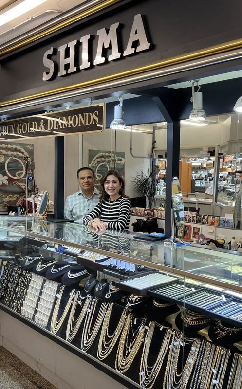 Two people stand behind a jewelry counter at SHIMA jewelry store.