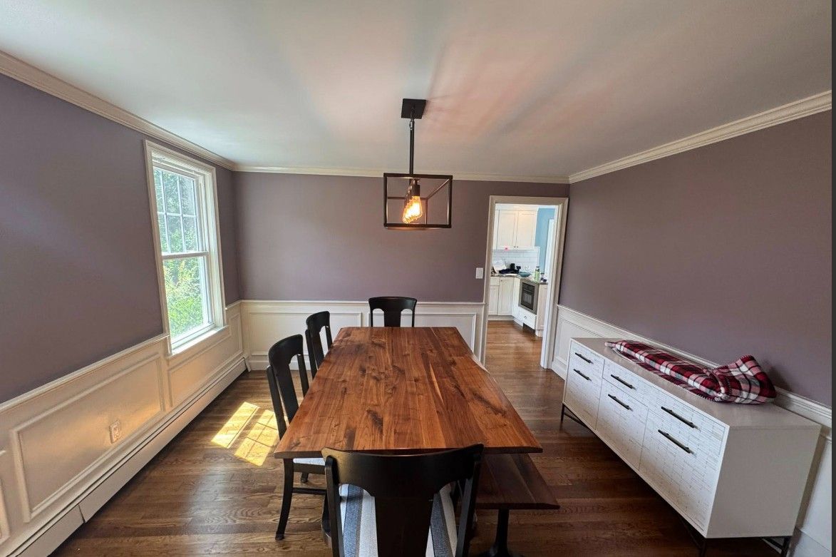 Dining room with long wooden table, black chairs, and white sideboard against purple walls.