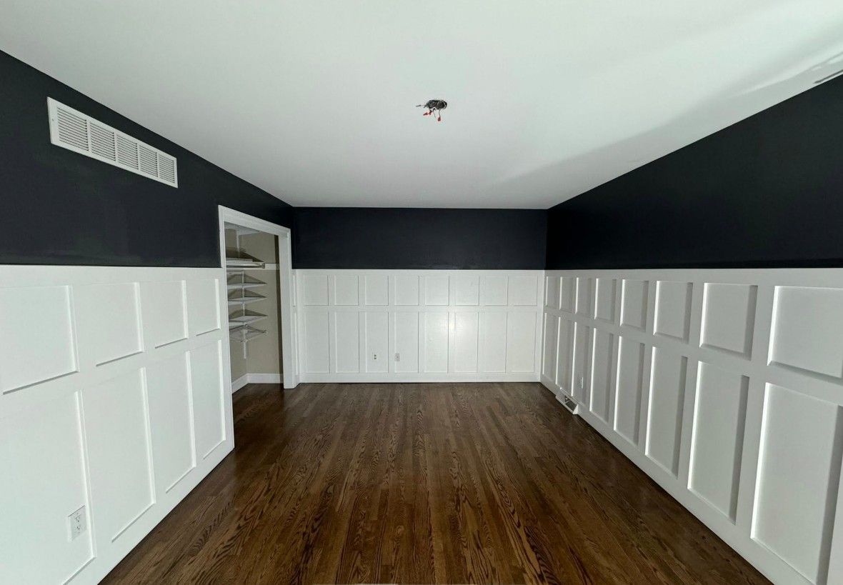 Room with dark blue upper walls, white wainscoting, and dark wood floors.