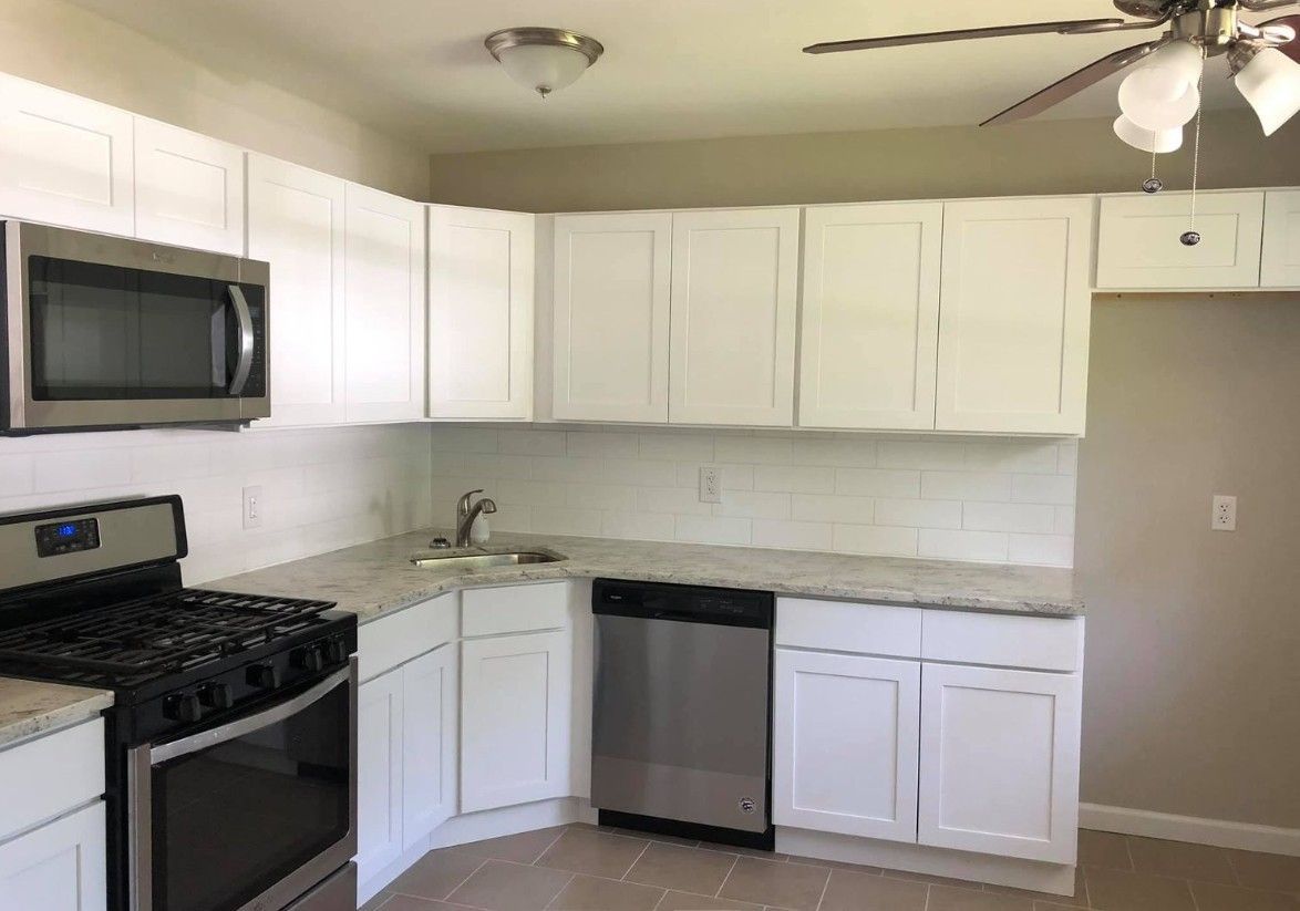 White kitchen with stainless steel appliances: microwave, stove, and dishwasher. White cabinets and light countertop.