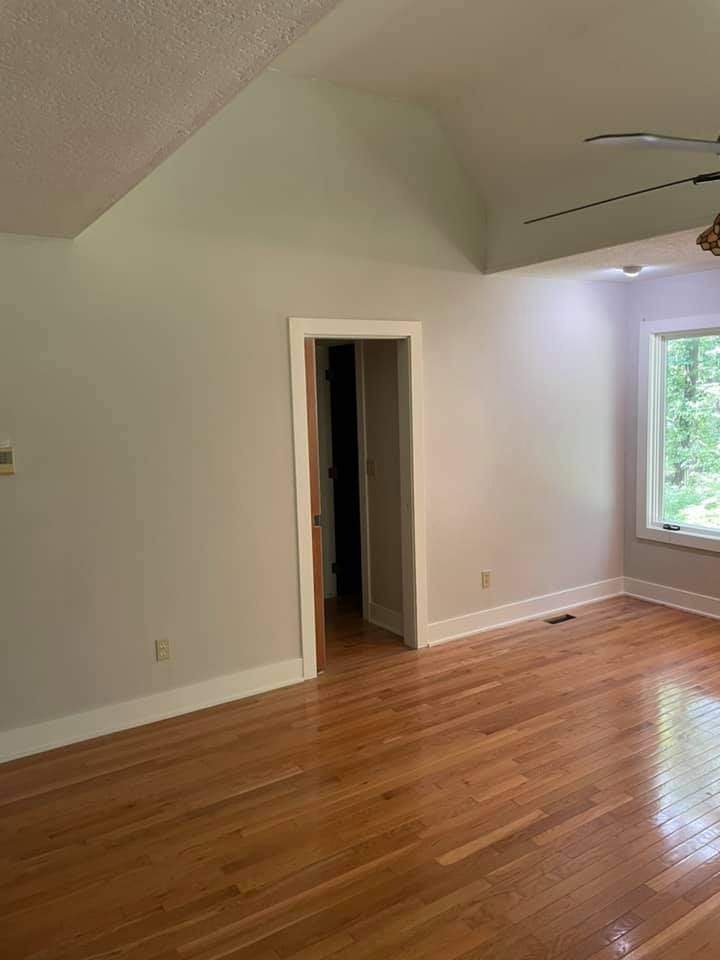 Bedroom with hardwood floors, a door, and a window. Light gray walls with white trim.