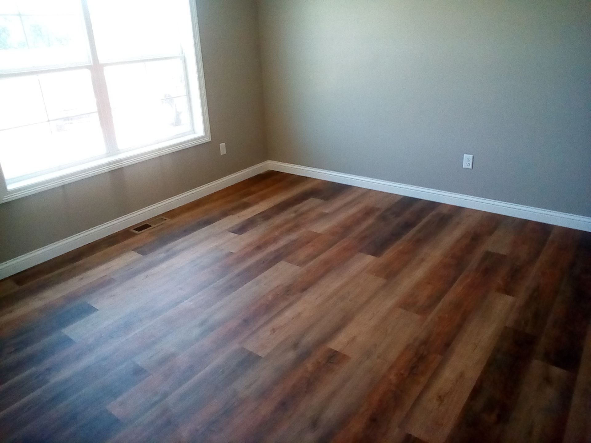 Empty room with hardwood-style flooring, gray walls, and a window.