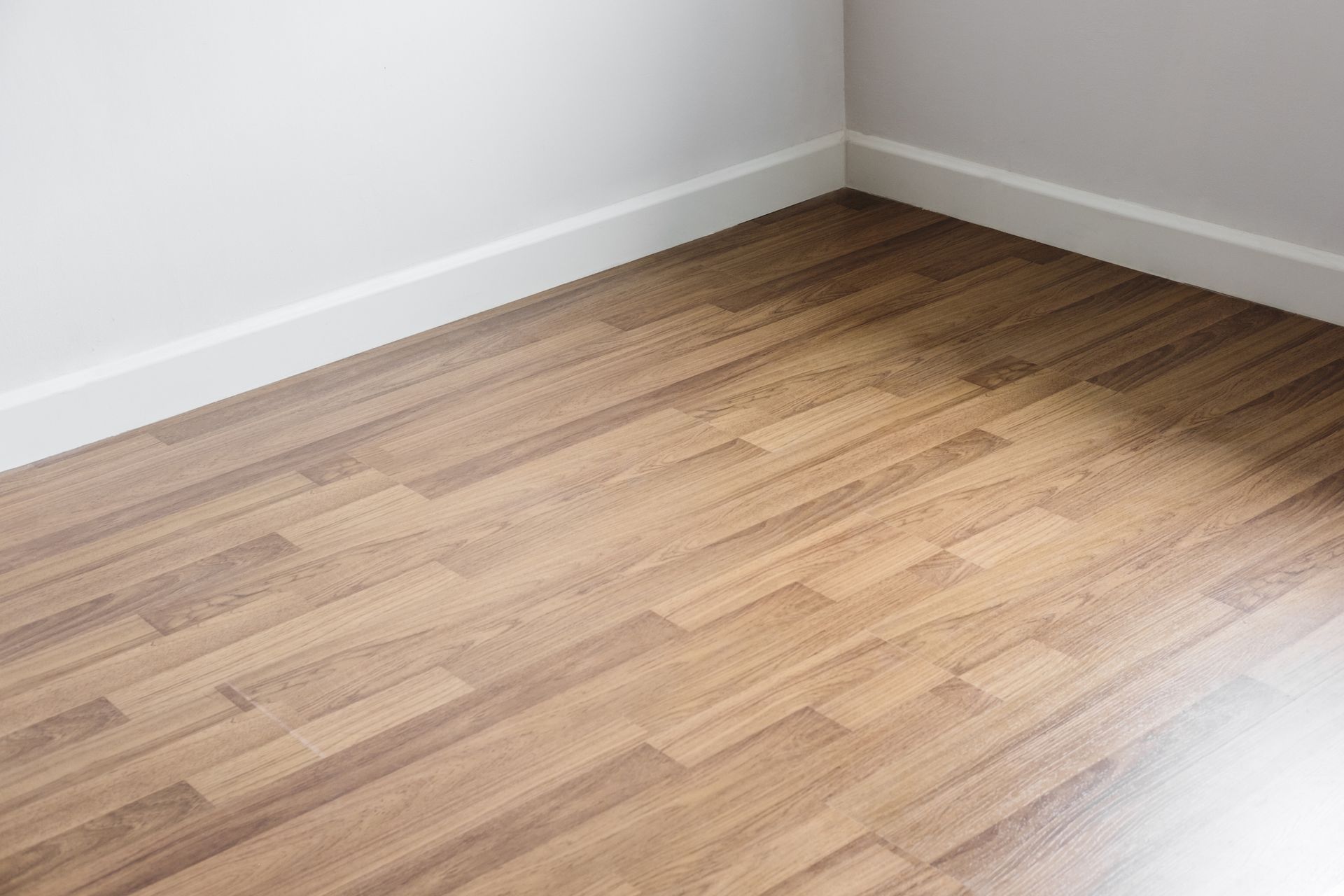 Corner of a room with wood flooring, white baseboards, and white walls.