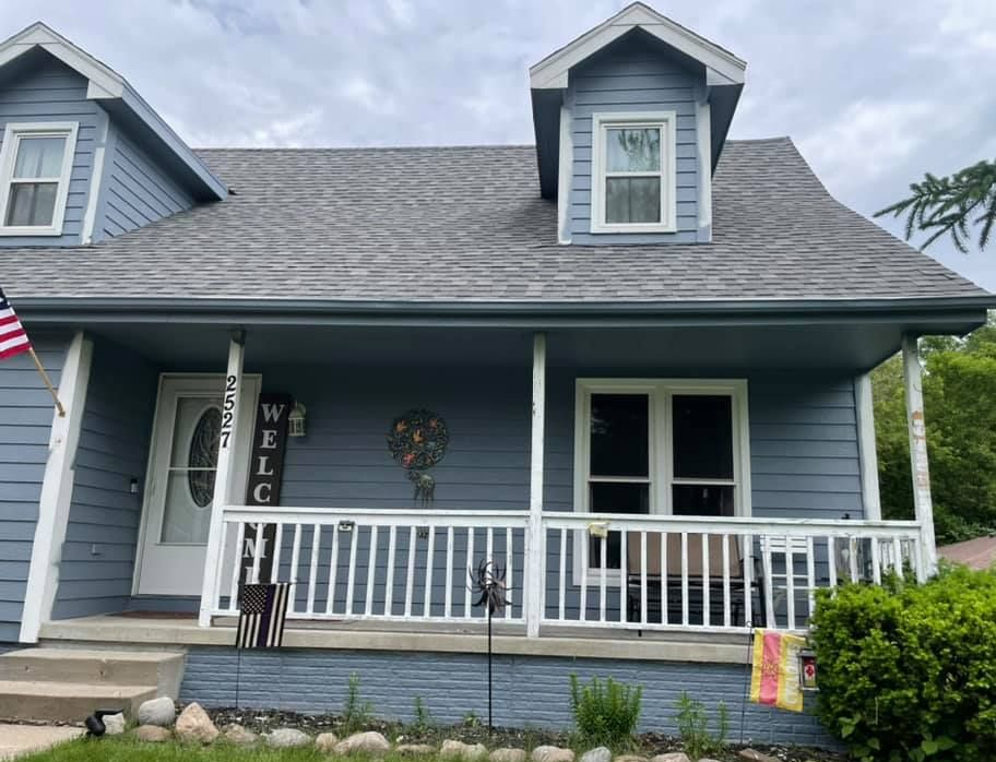 Blue house with white trim, porch, and a gray roof. American flag displayed.