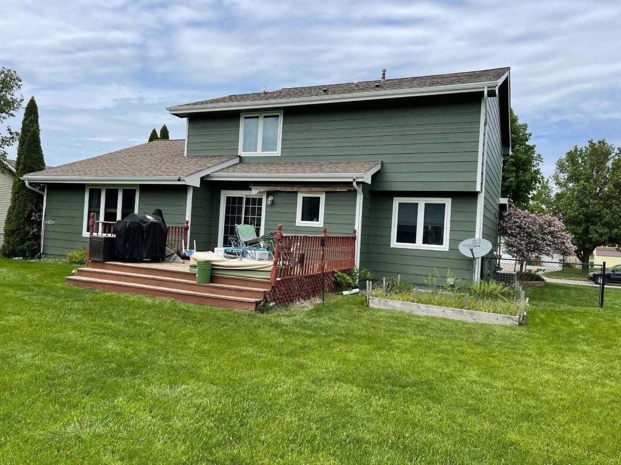 Green two-story house with a wooden deck and yard.