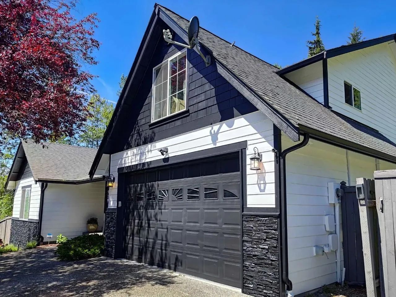 Black and white house with a garage, black garage door, stone accents, and a blue sky.