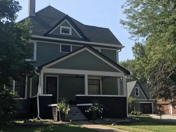 Two-story green house with porch, steps, and a small detached garage.